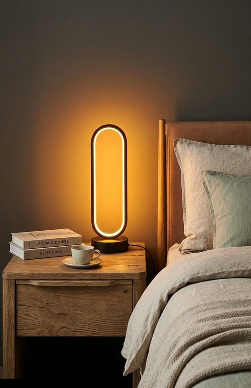 Lampe OVO — anneau LED ovale noir allumé sur une table de chevet